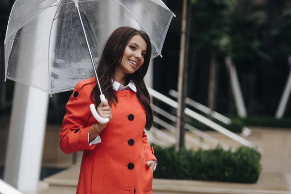 Retrato de mujer de una chica joven y bonita posando en la ciudad cogida de la mano en el bolsillo. Retrato de una joven sonriente con abrigo sosteniendo paraguas . — Foto de Stock
