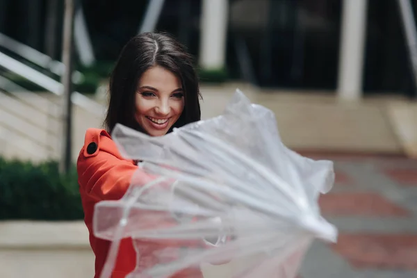 Outdoors portrait of beautiful young girl laughing opening closing umbrella. Portrait of stylish young smiling girl in red coat on city background. — Stock Photo, Image