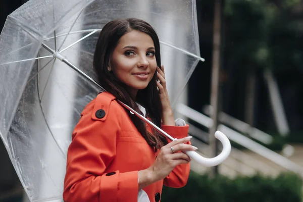 Mujer sonriente sosteniendo paraguas. Ella de pie en la calle después de la lluvia. Retrato de mujer joven con abrigo rojo sosteniendo paraguas . — Foto de Stock