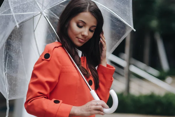 Brunette zakenvrouw het houden van een paraplu. Ze staat op straat na regen. Portret van jonge vrouw in rode vacht houden paraplu. — Stockfoto