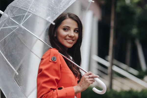 Mode foto van jong meisje poseren met paraplu. Ze staat op straat. Portret van jonge vrouw in rode vacht houden paraplu. — Stockfoto