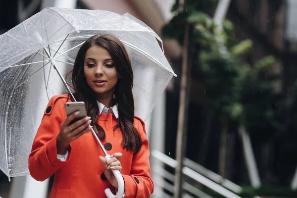 Business woman holding umbrella and texting from her cell phone near the office.