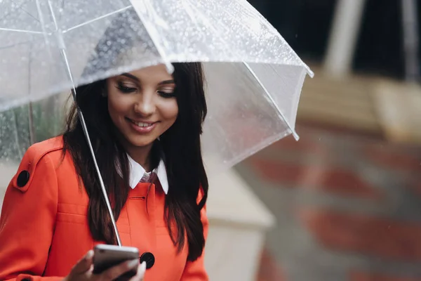 Portret van een gelukkige zakenvrouw texting op haar telefoon, het houden van paraplu. — Stockfoto