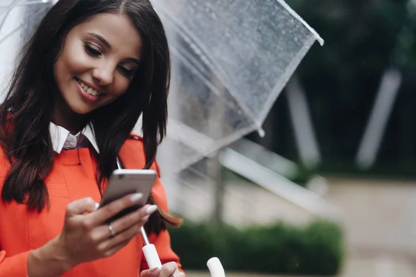 Portret van een vrouw met transparante paraplu het verzenden van tekstbericht van haar telefoon in stad. — Stockfoto