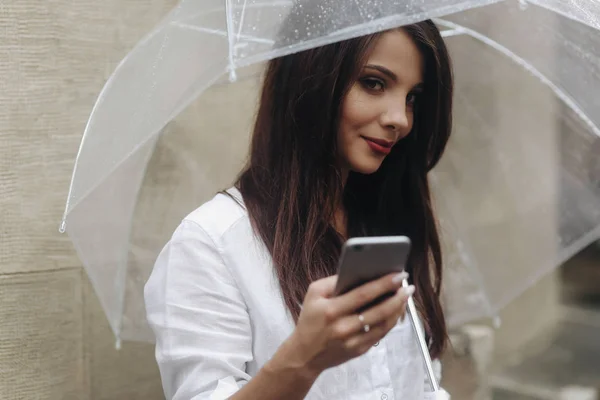 Close-up portret van een mooi meisje met paraplu noemt een vriend die op de straat stad staat. Het is zomer regen. — Stockfoto