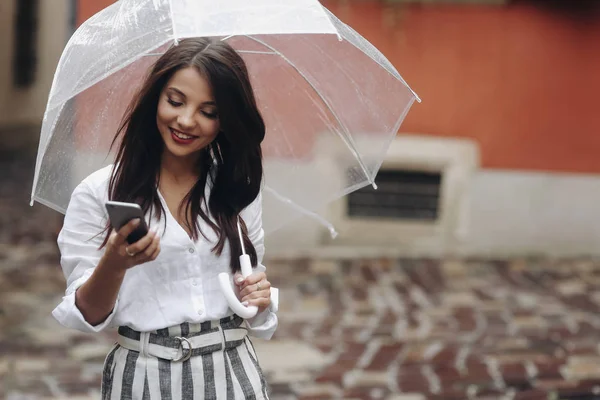 Portret van een mooi meisje met paraplu noemt een vriend die op de straat stad staat. Kopieer de ruimte aan de rechterkant. Het is zomer regen. — Stockfoto