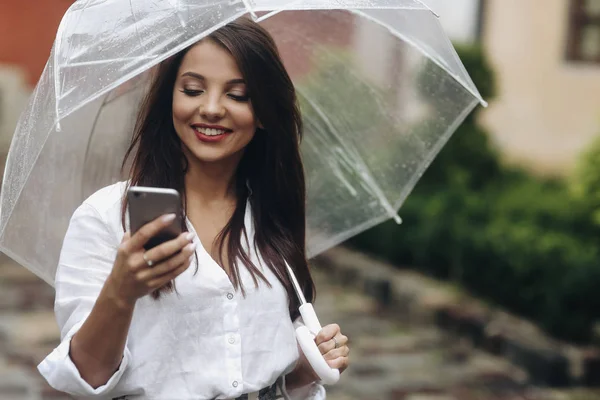 Portret van glimlachend mooi meisje met paraplu noemt een vriend die op de oude straat staat. Het is zomer regen. — Stockfoto