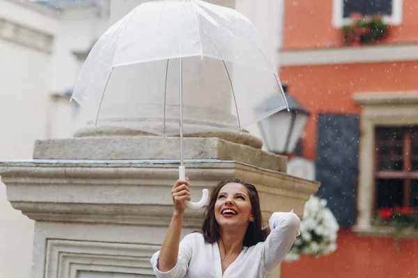 Mujer joven y feliz turista caminando por la calle de la ciudad bajo el paraguas, de pie cerca de la columna . — Foto de Stock