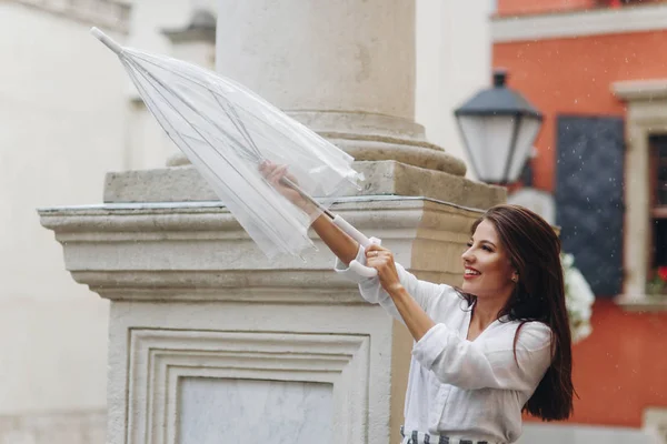 年轻和快乐的女游客走在城市的街道上，玩她的伞，站在附近的柱子. — 图库照片