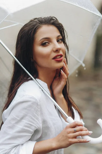 Enchanting young woman with umbrella walking around european city. It\'s summer rain.