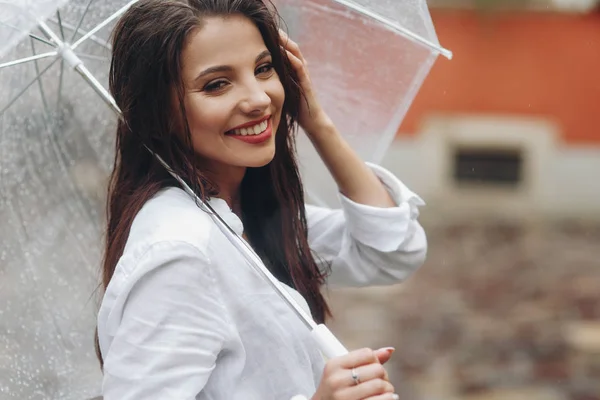 Jonge mooie meid met paraplu op een achtergrond van een stads straat in de zomerdag. Het is zomer regen. — Stockfoto