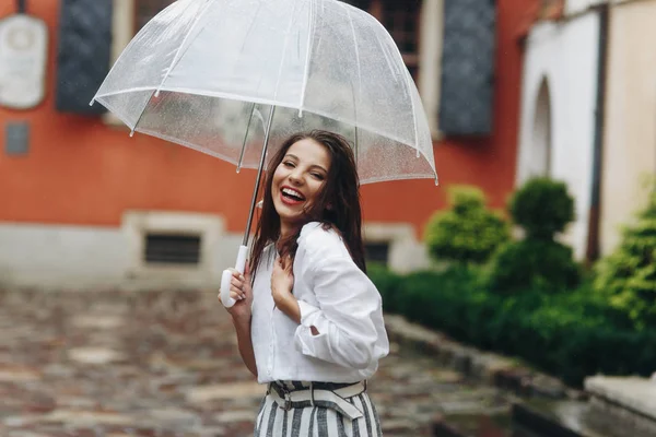 Encantadora chica morena con el pelo largo riendo y pasea por la ciudad en el día de verano. Es lluvia de verano. . —  Fotos de Stock