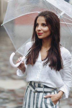 Eski evin yakınındaki bir şemsiye altında mutlu bir kadının dikey yakın portresi, kenara bakmak. Yaz yağmuru..