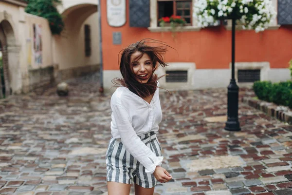 Emotionales Porträt einer fröhlichen schönen Frau mit langen Haaren, Mädchensprüngen, altem Straßenhintergrund. Modell blickt auf Kamera. — Stockfoto