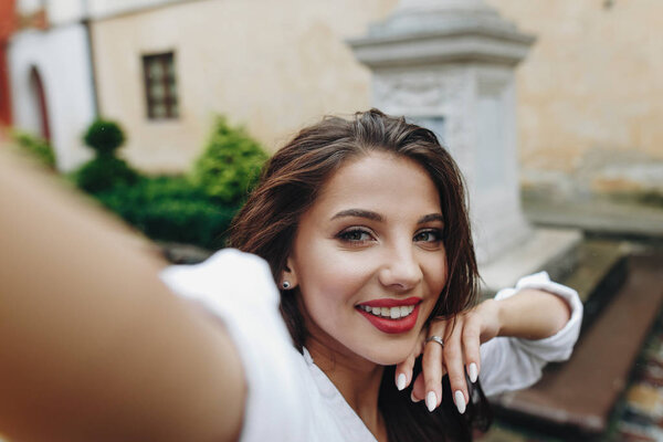 Close up horizontal pretty happy lovely smiling young woman making selphie with mobile phone on the background of street.