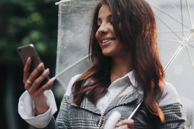 Onun erkek arkadaşı toplantı beklentisiyle güzel neşeli kadının yakın portresi. Şeffaf şemsiye altında gri ceket giyen kadın