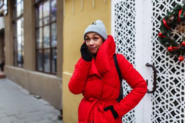 Sokağın arka planında cep telefonuyla konuşan bir kadın portresi. Kırmızı kış ceketli kadın kış gününde sokakta duruyor. Noel tatili konsepti. Sol taraftaki alanı kopyalama