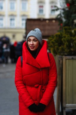 Noel Fuarı'nın arka planında durup kenara bakan güzel bir kadının portresi. Soğuk kış gününde sokakta duran kırmızı kış ceketli kadın. Noel tatili konsepti