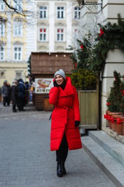 Noel Fuarı arka planda neşeli kadın portresi telefonda konuşurken. Kırmızı kış ceketli kadın kış gününde sokakta yürüyor. Noel tatili konsepti. Başın üstündeki alanı kopyalama