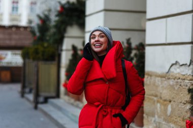 Noel Fuarı cep telefonu konuşurken arka planda gülen kadın portresi. Kırmızı kış ceketli kadın kış gününde sokakta duruyor. Noel tatili konsepti. Sol taraftaki alanı kopyalama