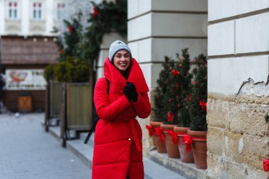 Noel Fuarı'nın yanında yürüyen neşeli bir kadın. Kırmızı kış ceketli kadın kış gününde sokakta yürüyor. Noel tatili konsepti. Sol veya sağ taraftaki alanı kopyalama