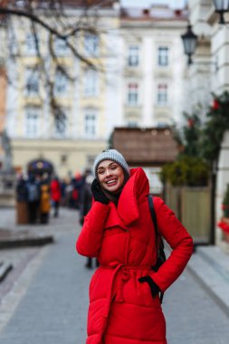 Neşeli kadın cep telefonu yla konuşurken Noel Fuarı arka planda duruyor. Kırmızı kış ceketli kadın kış gününde sokakta yürüyor. Noel tatili konsepti. Başın üstündeki alanı kopyalama