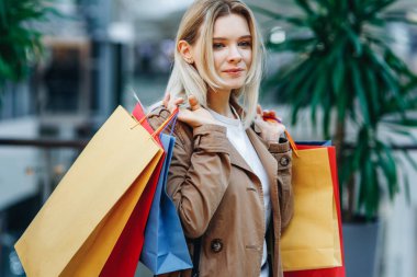 Alışverişten sonra güzel bir kadın. Bir alışveriş merkezinde kahverengi pelerinli genç kadının portresini kapatın. Alışveriş merkezinde renkli alışveriş poşetleri ile güzellik kadın. Alışveriş, satış, alışveriş merkezi