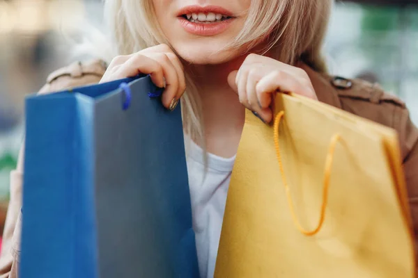 Close up portrait of woman with blue and yellow shopping bags at shopping mall. Bags in the foreground. The girl\'s face is not visible. Buying too much concept. Shopper, sales, shopping center