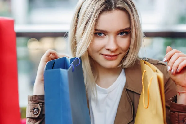 Shopogolic concept. Horizontal portrait of woman with blue and yellow shopping bags at shopping mall. Bags in the foreground. Buying too much concept. Shopper, sales, shopping center