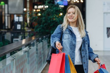 Alışveriş merkezinde çanta ile kot ceket güzel kız. O alışveriş ten sonra alışveriş çantaları taşıyor ve kenara bakıyor. Satış, mağaza, perakende konseptinde model. Sol taraftaki alanı kopyalama