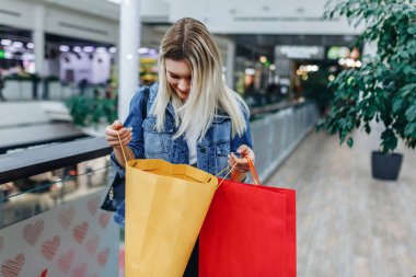 Ticaret ve alışveriş zamanı. Bulanık alışveriş merkezi arka planda çanta ile kot ceket güzel kız. Alışveriş çantasına bakan bir kadın. Sağ taraftaki alanı kopyalama