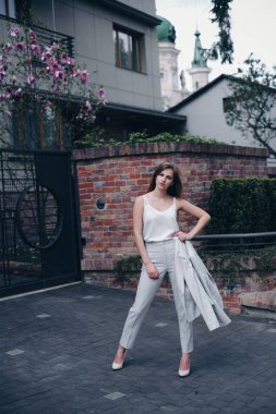 Yumuşak beyaz hatlı çekici bayan öğrenci şık bir takım elbise giyiyor ve bahçeli ofisin yanındaki kaldırımda duruyor. Kadın elini beline koydu ve özgüvenle kameraya baktı. Arka planda şehir manzaraları. Fas kavramı