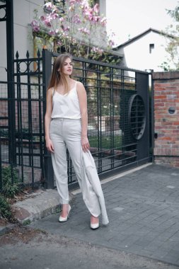 Klasik açık renk takım elbiseli beyaz bir kadının kaldırımda dikilip bakışlarını kaçırması. Makyajlı, kalın görünüşlü ve ceketini tutan ince sarışın kadın. Moda ve iş anlayışı.