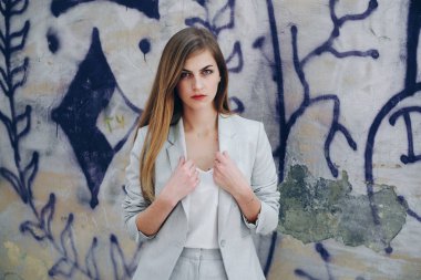 Uzun düz saçlı, açık renk takım elbiseli, kameraya bakan çekici bir kadın. Ceketini düzelten derin görünüşlü bir manken. Moda ve iş anlayışı.