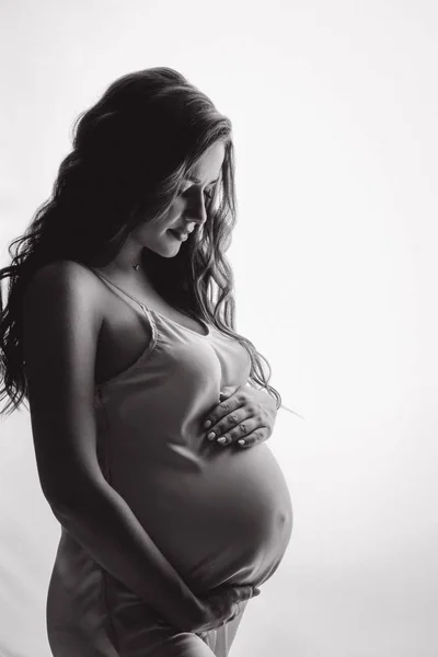 長波の髪をしたサテンのドレス姿の妊婦さんのフロントビュー 母親は彼女の胃を抱き それを見ています 愛と母権の概念 — ストック写真