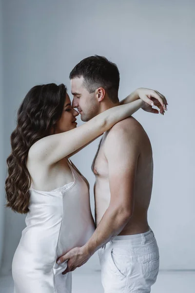 夫と妊婦のスタジオ撮影 ブルネットの長い髪をした白人女性は彼女の男を抱きかかえた 男性は彼女の鼻にキスをし 彼女の胃に触れる 愛と父母の概念 — ストック写真
