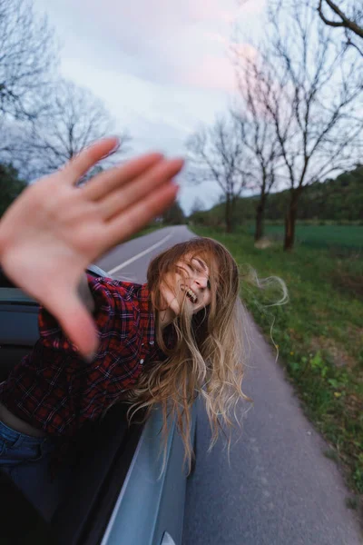 Bella ragazza bionda salito dal finestrino della macchina, guarda e cattura il vento — Foto Stock