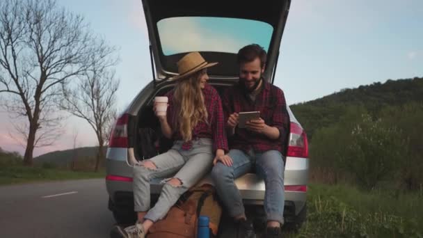 Paar sitzt im Kofferraum des Autos und staunt über Foto auf Tablet — Stockvideo