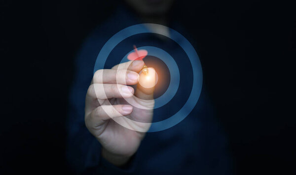 Business success concept with businessman hand holding dart hitting glowing target, symbolizing goal achievement, focus, strategy, and ambition. Perfect for corporate vision and growth theme