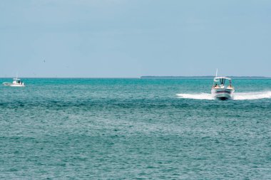 White motorboat with blue and red stripe speeding towards shore on blue water