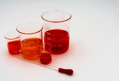 Dört bilim beher turuncu ve kırmızı sıvı ile kırmızı bir ampul ile bir damlalık ile beyaz bir arka plan üzerinde ekranın sol tarafına ayarlanmış