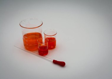 Üç bilim beherturuncu ve kırmızı sıvı ile kırmızı bir ampul ile bir damlalık ile beyaz bir arka plan üzerinde ekranın sol tarafına ayarlanmış