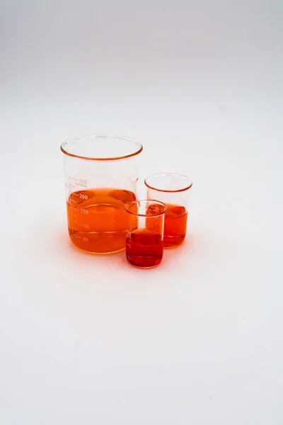 白い背景の画面の右側に設定されたオレンジと赤の液体で満たされた3つの科学ビーカーの垂直画像 — ストック写真