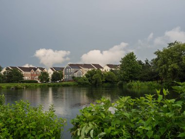 Bereketli yeşil yapraklı sakin bir gölet, banliyö evleri ve Ashburn, Virginia 'da bulutlu bir gökyüzü yansıtıyor..