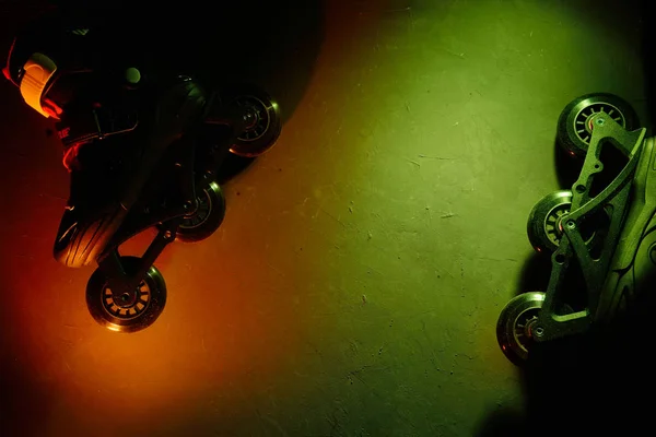 Vista de cerca de los patines de ruedas en línea o patinaje sobre fondo grunge oscuro en luz verde amarilla azul neón —  Fotos de Stock