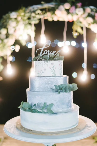 Decorated by flowers multilevel wedding cake with lights on the background