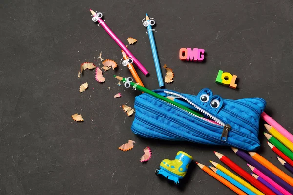 Funny Back to School concept - pencil case eating pencils on black chalk background. Space for text.