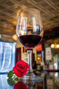 Yarım dolu bir şarap kadehinin tabanında tek bir kırmızı gülle bir barda otururken düşük açılı görüntüsü.