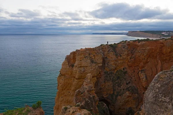 Atlantik Okyanusu, Algarve, Portekiz bir kıyı şeridi üzerinde bulutlu gün batımı. Gün batımında kıyı uçurumun kıyısında yalnız bir balıkçı.