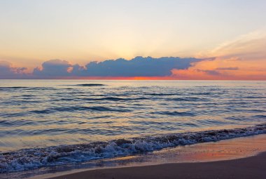 Boş bir kumsalda haddeleme bulutlu gün doğumu ve deniz dalgaları. Güneş bulutların üzerinde zamanlarda İspanya'nın Valencia bölgesinde Akdeniz üzerinde görünür.